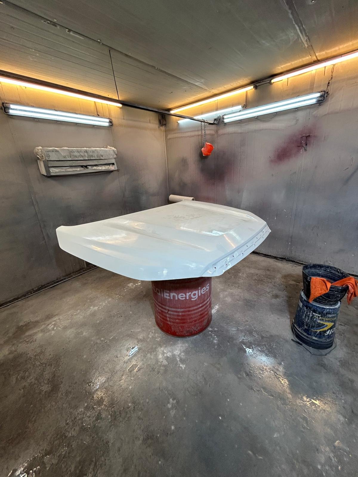 Capot recién pintado, apoyado sobre un tambor en la cabina de pintura